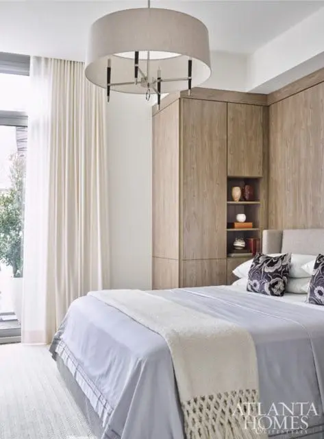 Bedroom with a large drum pendant light, light grey bedding, and built-in wood-grain cabinetry with open shelving displaying decorative vases and books.
