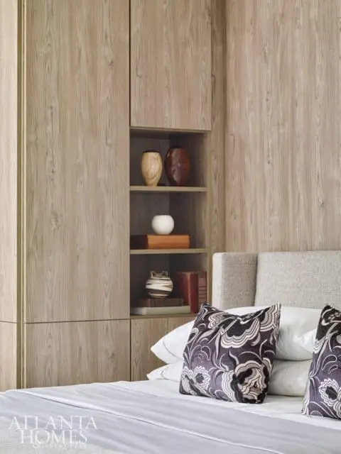 Bedroom with built-in wood-grain cabinetry, open shelving displaying decorative vases and books, and a bed with patterned pillows.
