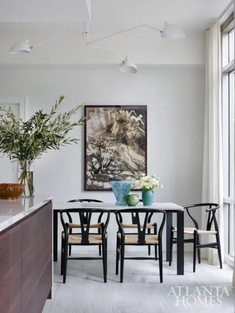 Dining area with a marble-top table, black wishbone chairs, and abstract art on the wall. A modern white chandelier hangs overhead.