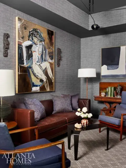 Living room with textured gray walls, featuring a brown leather sofa, blue upholstered armchairs, a large abstract painting of a nude, and a black coffee table.