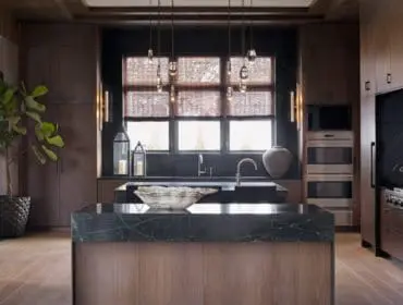 Dark wood kitchen with a large island topped with black marble, stainless steel appliances, and pendant lighting above the sink.