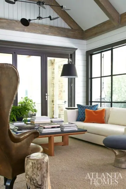 Living room with a white sofa, leather wingback chair, dark wood coffee table stacked with books, and a black pendant light.