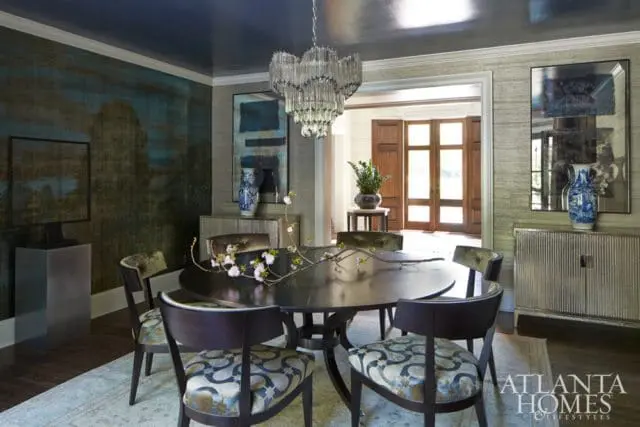 Dining room with dark oval table, upholstered chairs, textured wallpaper, abstract art, and a crystal chandelier.