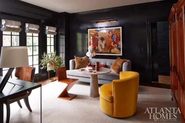 Dark gray room with a gray sofa, round marble table, and yellow velvet armchair. Artwork hangs above the sofa.