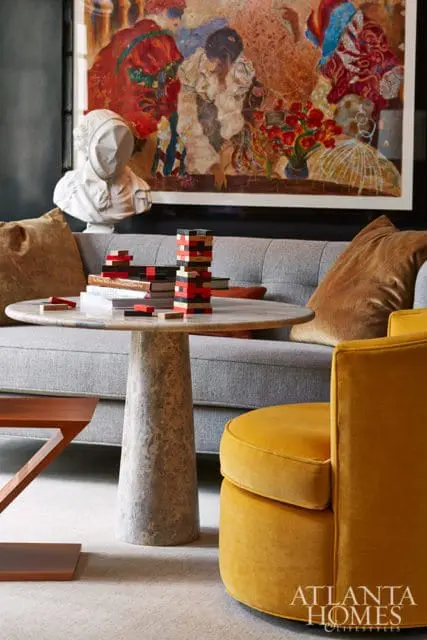 Living room with gray sofa, marble pedestal table with stacked books and Jenga game, and a yellow velvet swivel chair.