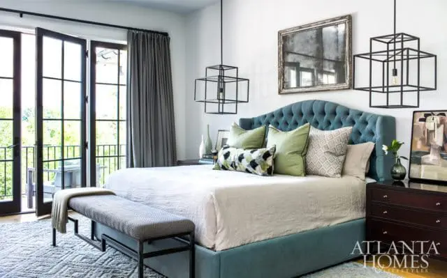 Bedroom with a teal tufted headboard, light beige bedding, green and patterned accent pillows, a dark wood dresser, and a black metal bench at the foot of the bed.