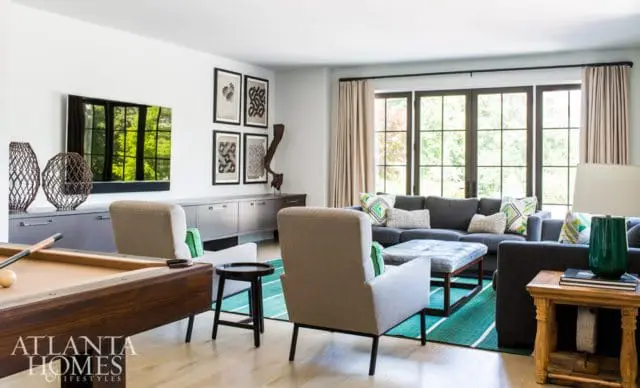 Living room with a grey sectional sofa, two armchairs, a pool table, and a large window overlooking greenery.
