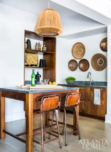 Kitchen island with dark stone countertop and wooden base, two leather bar stools, and a built-in wooden shelving unit displaying decorative items.