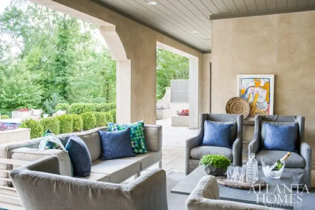 Covered patio with gray upholstered sofa and armchairs, blue and green patterned pillows, and a stone coffee table with drinks.
