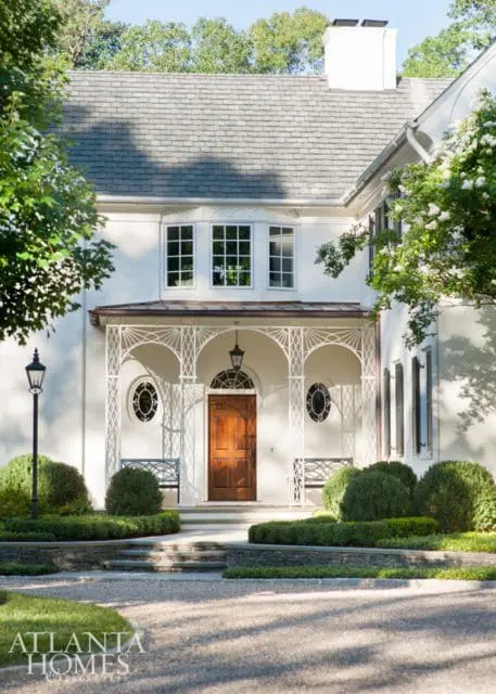 White house with a wooden front door, arched porch with decorative metalwork, and manicured landscaping.