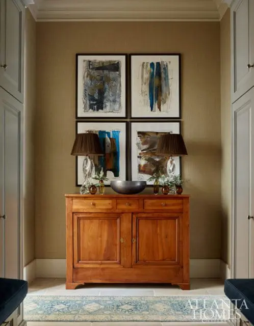 Hallway with textured tan walls, a wooden credenza topped with abstract art and lamps, and a blue and white patterned runner on a stone floor.
