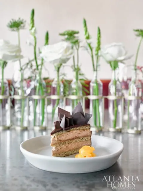 Slice of chocolate mousse cake with chocolate shards on top, served on a white plate with a dollop of orange garnish.