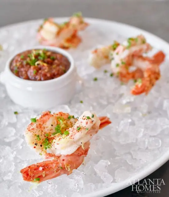 Close-up of cooked shrimp seasoned with herbs and spices, served on crushed ice with a small bowl of dipping sauce.