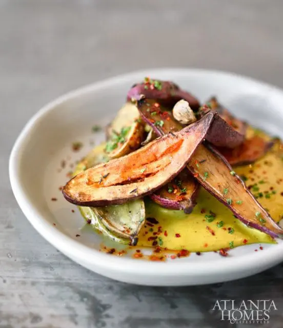 Roasted eggplant slices and wedges served with a yellow sauce and sprinkled with herbs and red pepper flakes on a white plate.