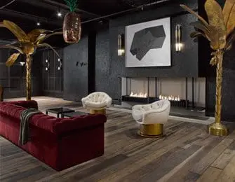 Living room with dark textured walls, a red velvet tufted sofa, two white swivel chairs with gold bases, and gold palm tree floor lamps. A modern fireplace is centered on the wall above abstract art.