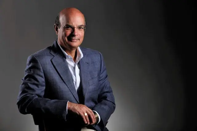 Bald man in glasses wearing a blue plaid suit jacket and white shirt, smiling.
