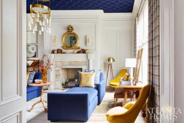Living room with a navy blue geometric ceiling, white paneled walls, a marble fireplace, and a navy blue chaise lounge.