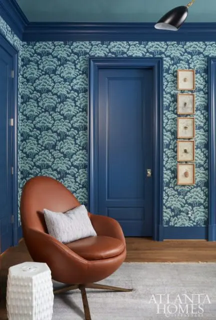 Blue room with tree-patterned wallpaper, a brown leather swivel chair with a striped pillow, and framed insect specimens on the wall.
