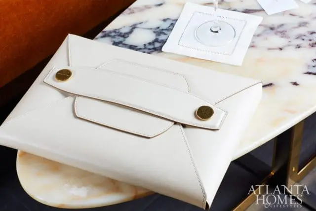 Close-up of a white leather clutch with gold hardware resting on a marble-topped table next to a cocktail glass and coaster.