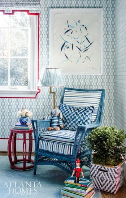 Blue wicker armchair with striped cushions and a patterned pillow, next to a red side table and a plant in a geometric basket.