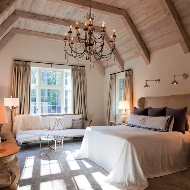 Master bedroom with vaulted wood-beamed ceiling, large window, tufted headboard, and ornate chandelier.