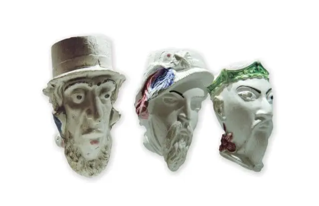 Three decorative ceramic busts of faces, each with a different hat and beard, against a white background.