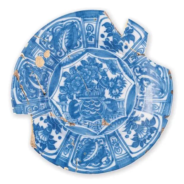 Fragment of a blue and white ceramic plate with floral and bird motifs, showing visible cracks and chips.