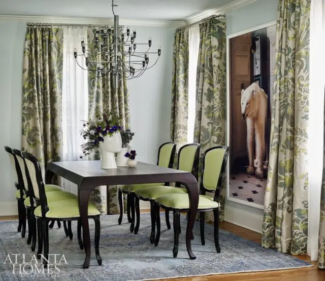 Dining room with dark wood table, green upholstered chairs, patterned curtains, and a large framed artwork of a polar bear.