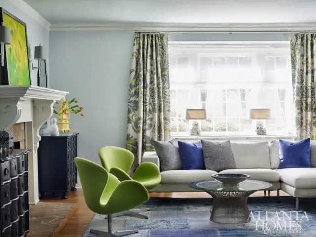 Living room with a light blue wall, white sectional sofa with blue and gray pillows, two lime green chairs, a glass coffee table, and a fireplace with a black chest.