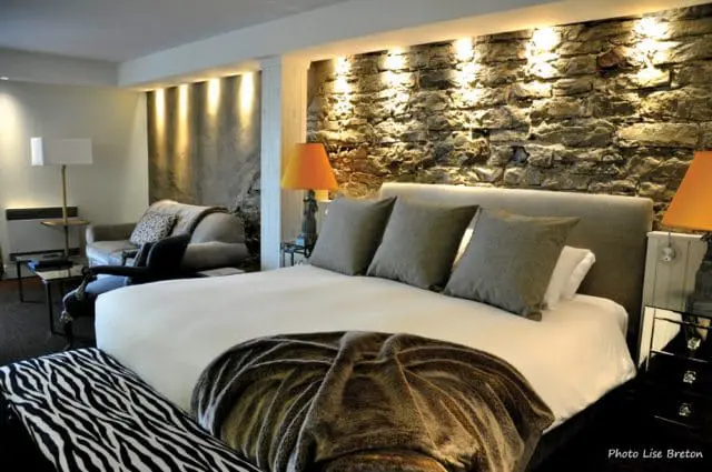 Bedroom with a king-size bed, grey headboard, and stone accent wall. Includes a grey sofa, orange lamp, and zebra-print bench.