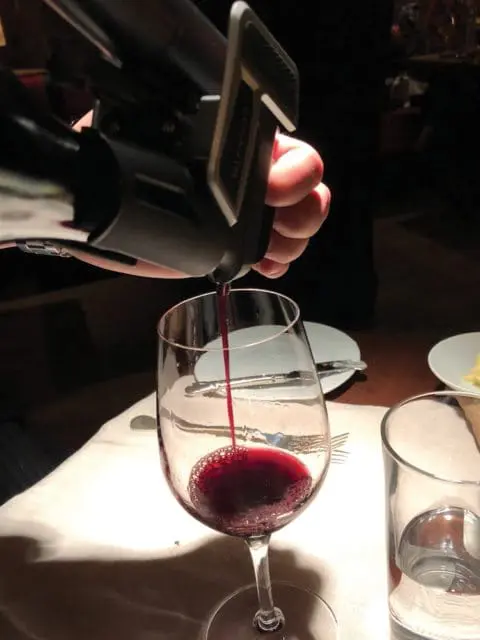 Coravin wine preservation system pouring red wine into a glass on a table set for a meal.