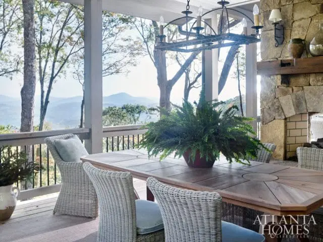 Covered porch with a wooden dining table and chairs, stone fireplace, and mountain view.