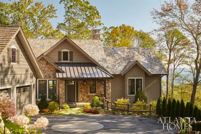 Craftsman-style house with stone and wood siding, metal roof, and a covered porch. Surrounded by trees and a mountain view.