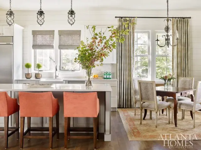 Kitchen and dining area with coral bar stools at a white island, and a dark wood dining table with leopard print chairs.