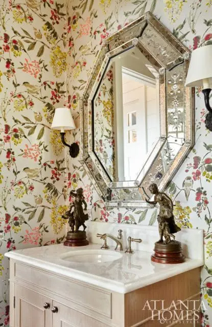 Powder room with floral wallpaper, marble vanity, ornate octagonal mirror, and bronze figurines on the countertop.