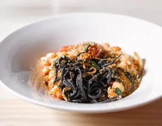 Close-up of black squid ink pasta with shrimp and breadcrumbs in a white bowl