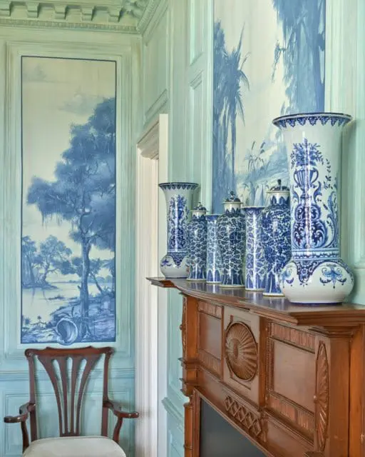 Blue and white chinoiserie vases displayed on a wooden mantelpiece with carved details. A tall framed mural of a landscape scene hangs on the wall to the left.