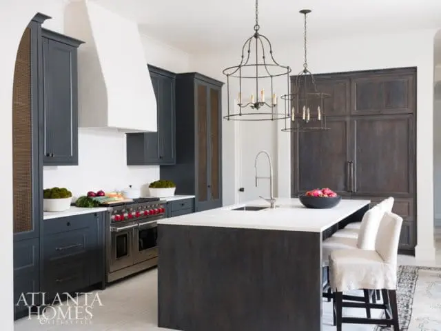 Dark gray kitchen cabinets with white quartz countertops, a stainless steel range, and a large island with pendant lighting.