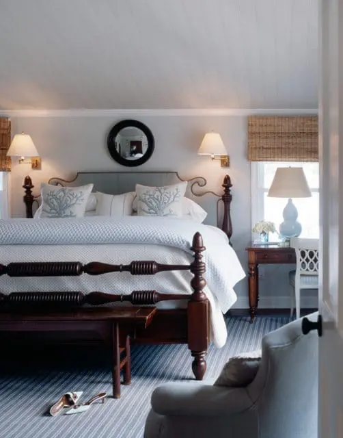 Master bedroom with a dark wood spindle bed, light blue upholstered headboard, white bedding with coral-patterned pillows, and a striped blue and white rug.