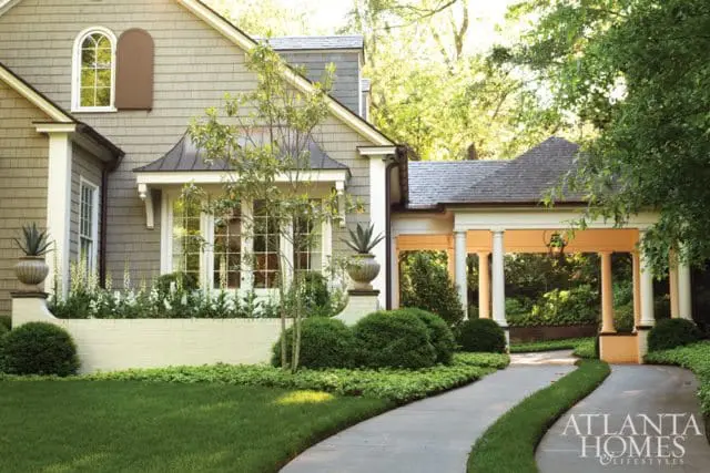 Traditional home with gray shake siding, arched window, white brick planter, and covered porch with columns.