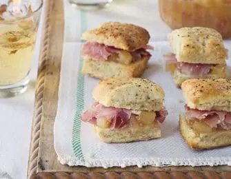 Four small savory biscuits filled with ham and a light-colored spread, served on a white cloth with a green stripe.