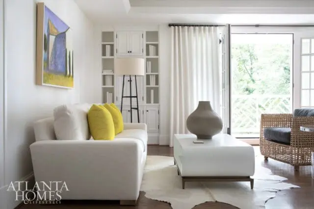 White sectional sofa with yellow accent pillows, white coffee table with ribbed vase, and built-in white shelving unit.