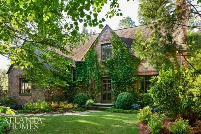 Brick house with ivy climbing the facade, a gabled roof, and lush green landscaping with a stone pathway.