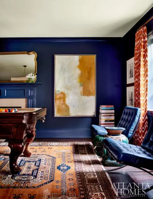 Dark blue room with a wooden pool table, ornate rug, abstract painting, and navy leather chairs.