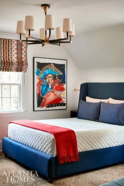 Bedroom with a navy blue upholstered bed, white quilted comforter, red throw blanket, and a framed portrait of Napoleon Bonaparte.