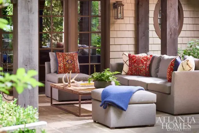 Covered patio with gray sectional sofa, ottoman, wooden coffee table with antlers, and patterned throw pillows.