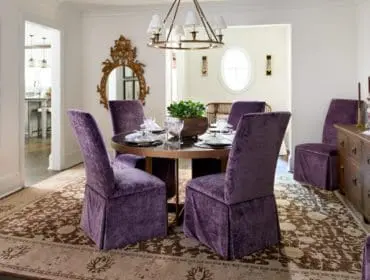 Dining room with plush purple velvet chairs around a round table, a dark wood buffet with decorative items, and a large landscape painting on the wall.