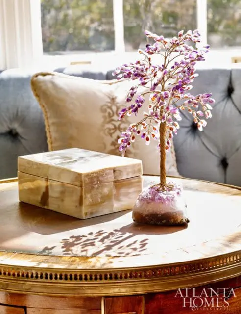 A decorative beaded tree with purple and clear beads sits on an amethyst geode base next to a mother-of-pearl box on a wooden table.
