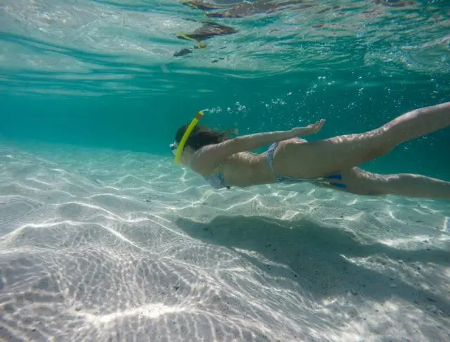 Woman snorkeling underwater over a sandy seabed with sunlight patterns on the sand.