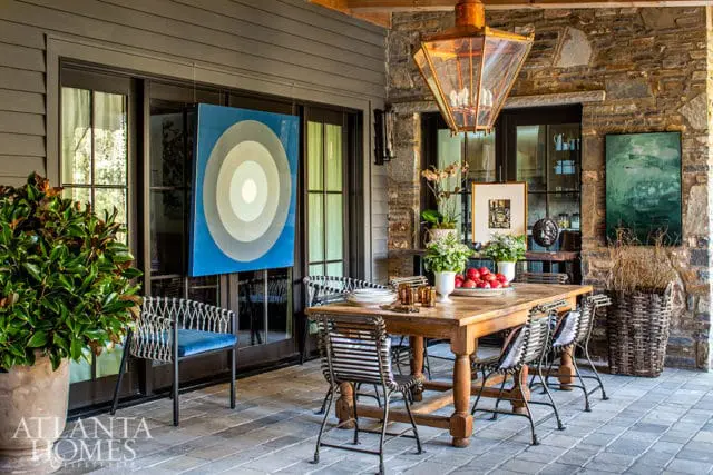 Covered patio with a wooden dining table and chairs, a large blue abstract painting, and stone accent walls.